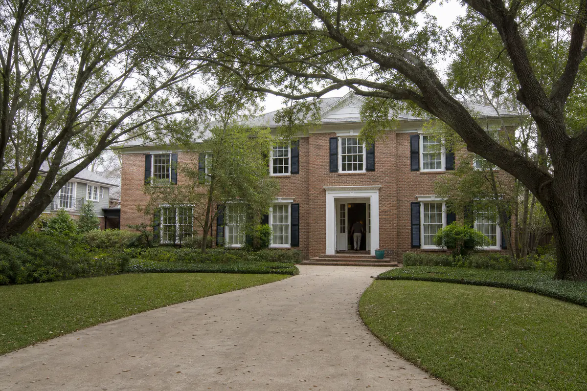 A large brick home set back under old oak trees at the end of a wide driveway