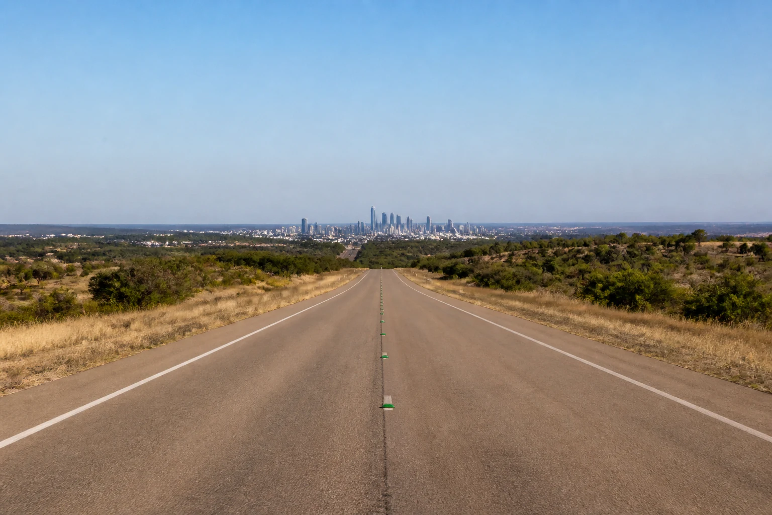 A two lane Texas highway running straight toward a distant city skyline